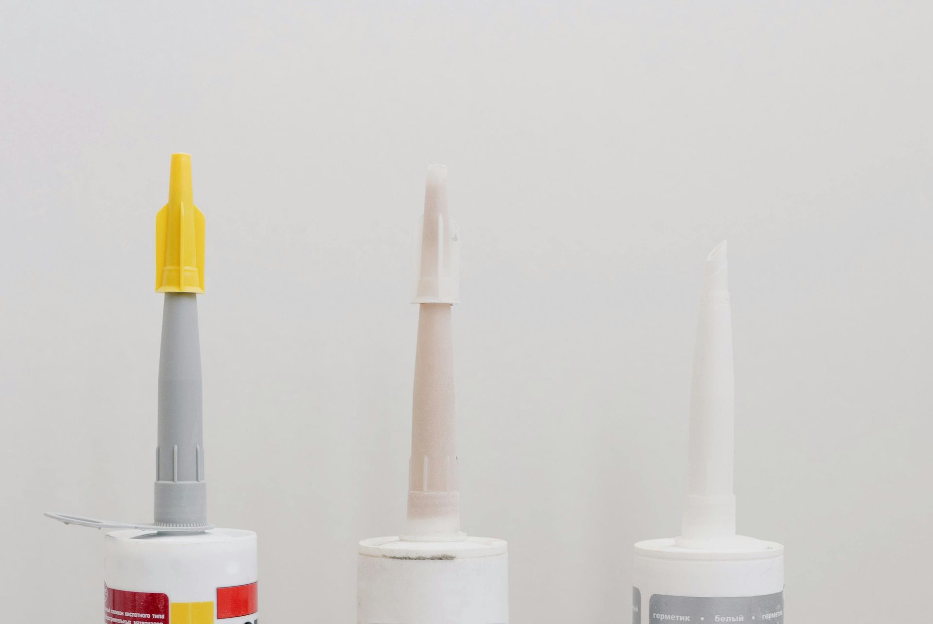 Three tubes of sealant with different colored nozzles against a white background.