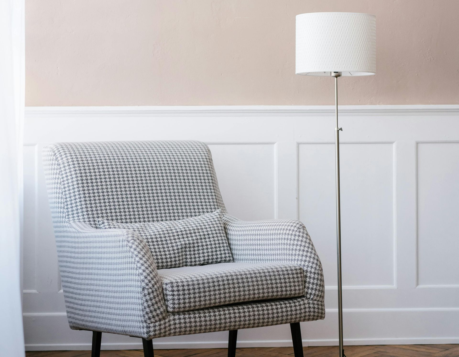 Armchair with patterned fabric, small pillow, and floor lamp next to a wainscoted wall.