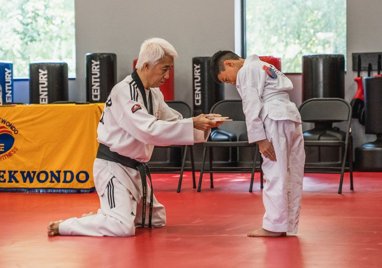 A man is kneeling down next to a young boy in a taekwondo class.