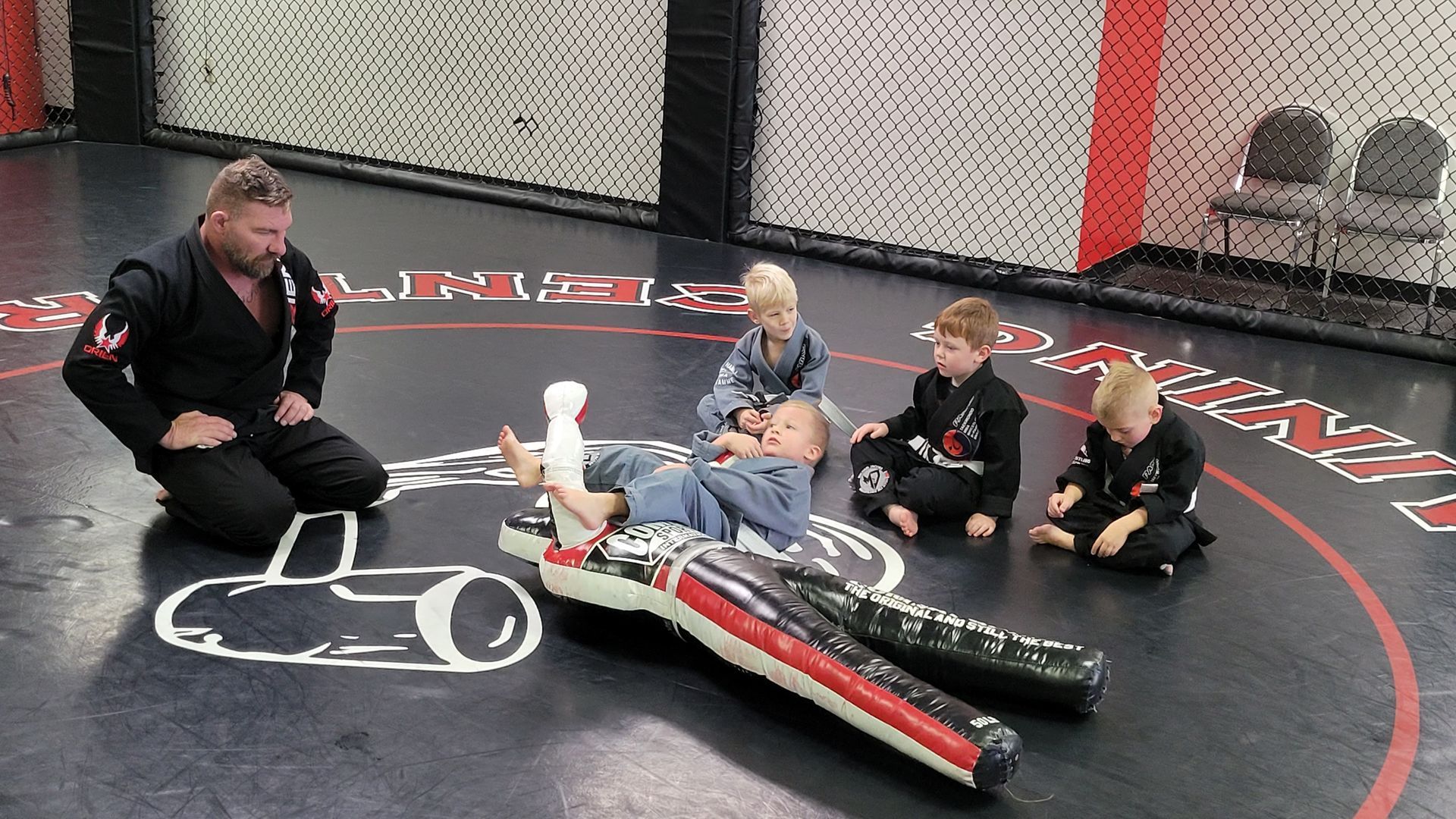 A group of young boys are sitting on the floor in a gym.