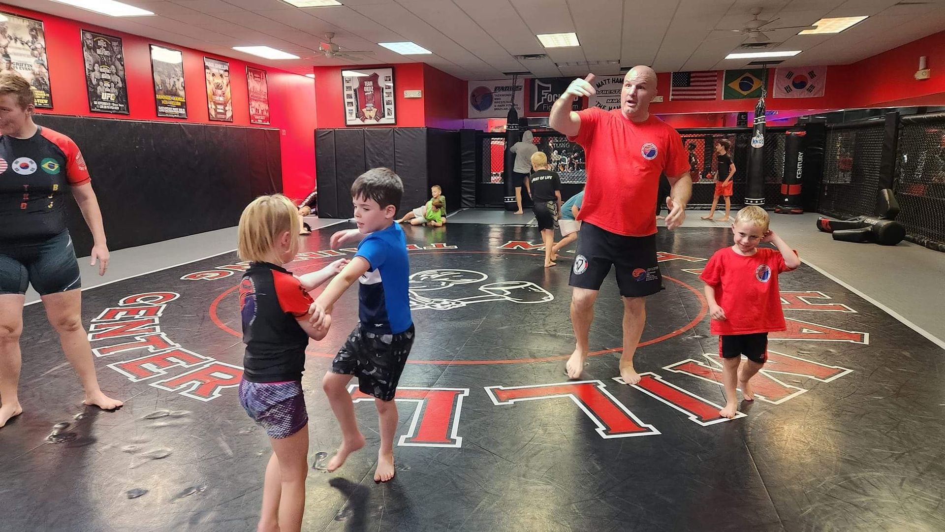 A group of people are standing on a wrestling mat in a gym.