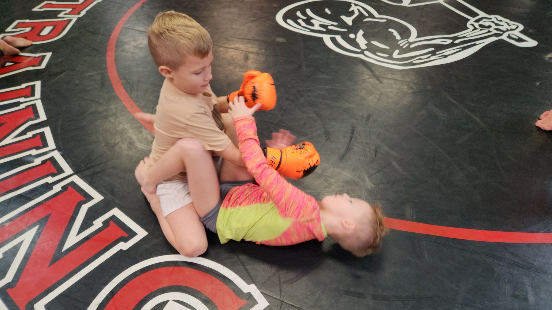 A boy and a girl are wrestling on a wrestling mat.