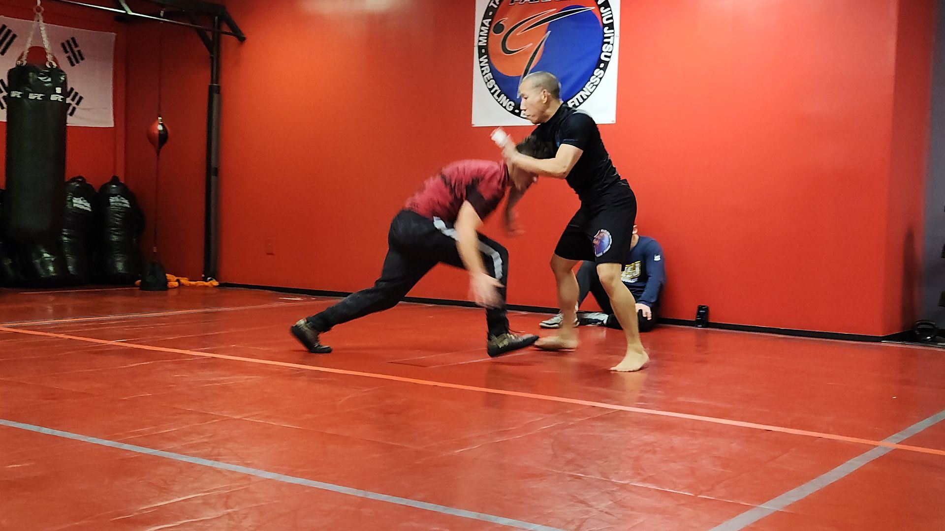 Two men are wrestling in a gym on a red mat.