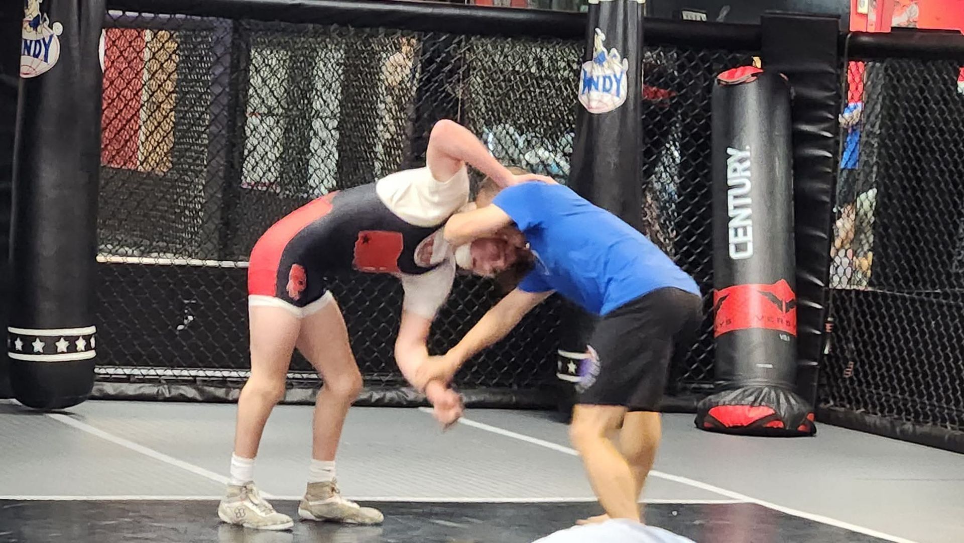 Two men are wrestling in a cage in a gym.