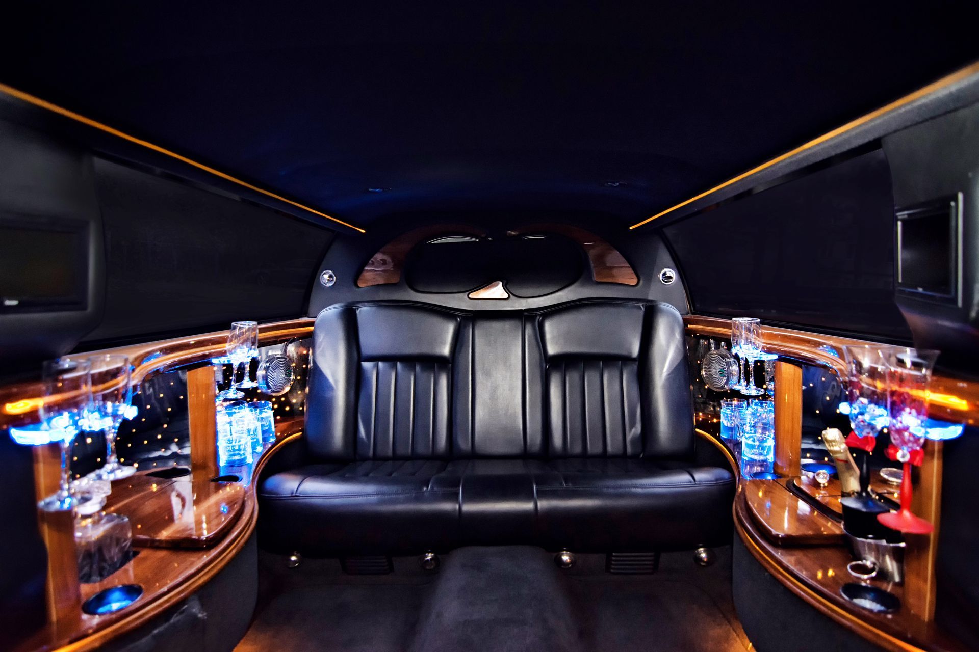 Interior of a limousine with black leather seating, bar, and blue accent lighting