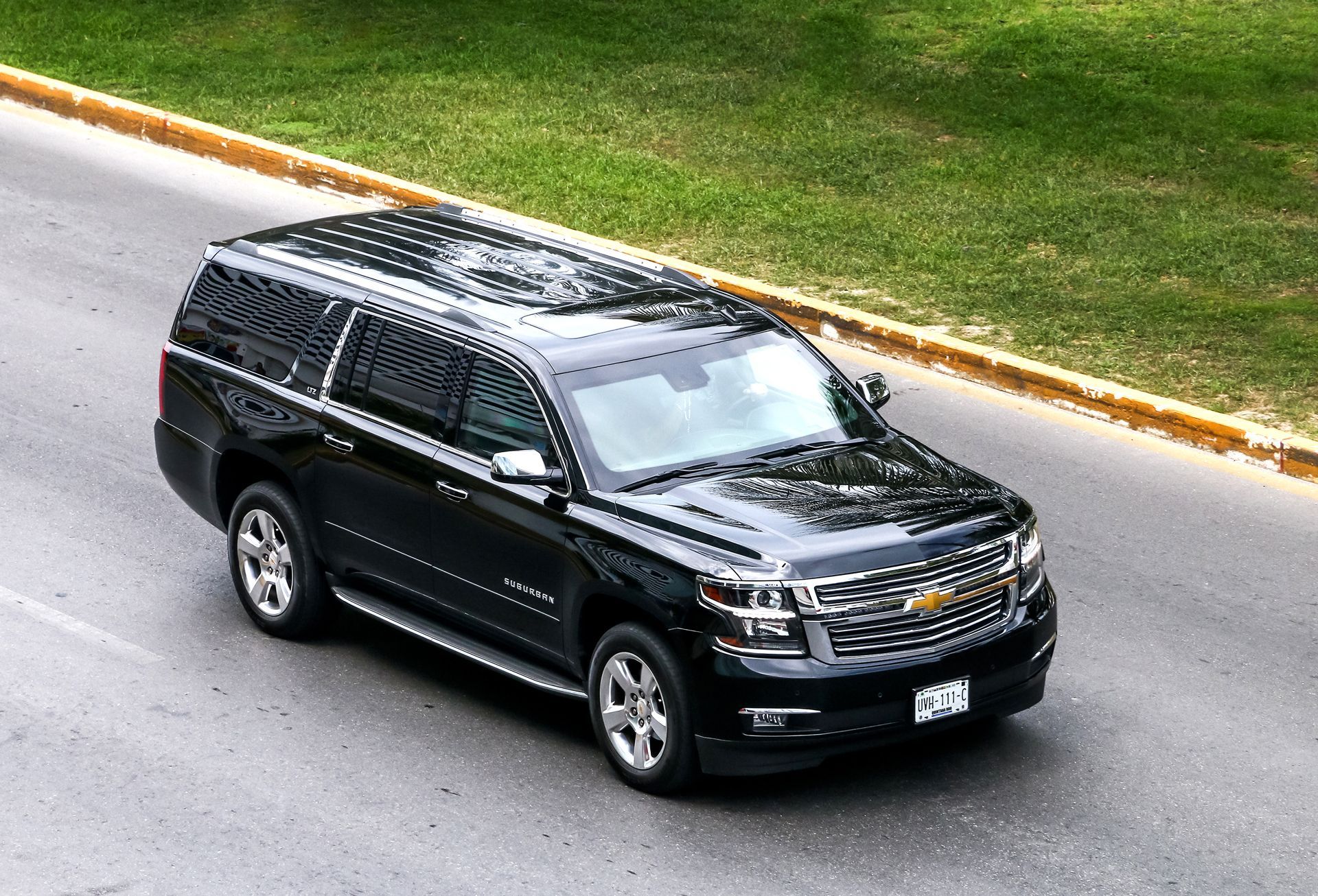 Black Chevrolet Suburban SUV driving on a paved road near green grass