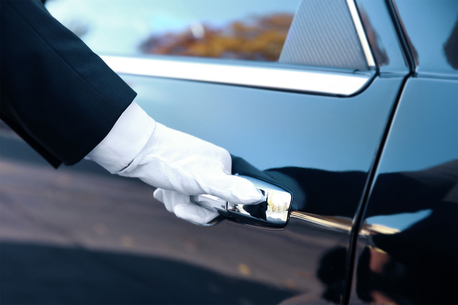A gloved hand opens a black car door with a key, likely a chauffeur