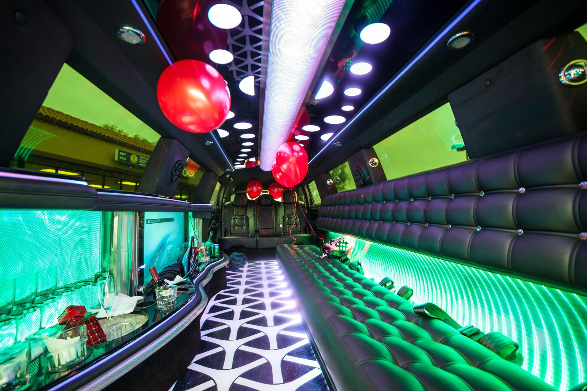 Interior of a limousine with black leather seating, vibrant LED lights, and red balloons