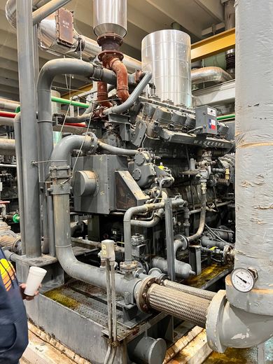 A man is standing next to a large engine in a factory.