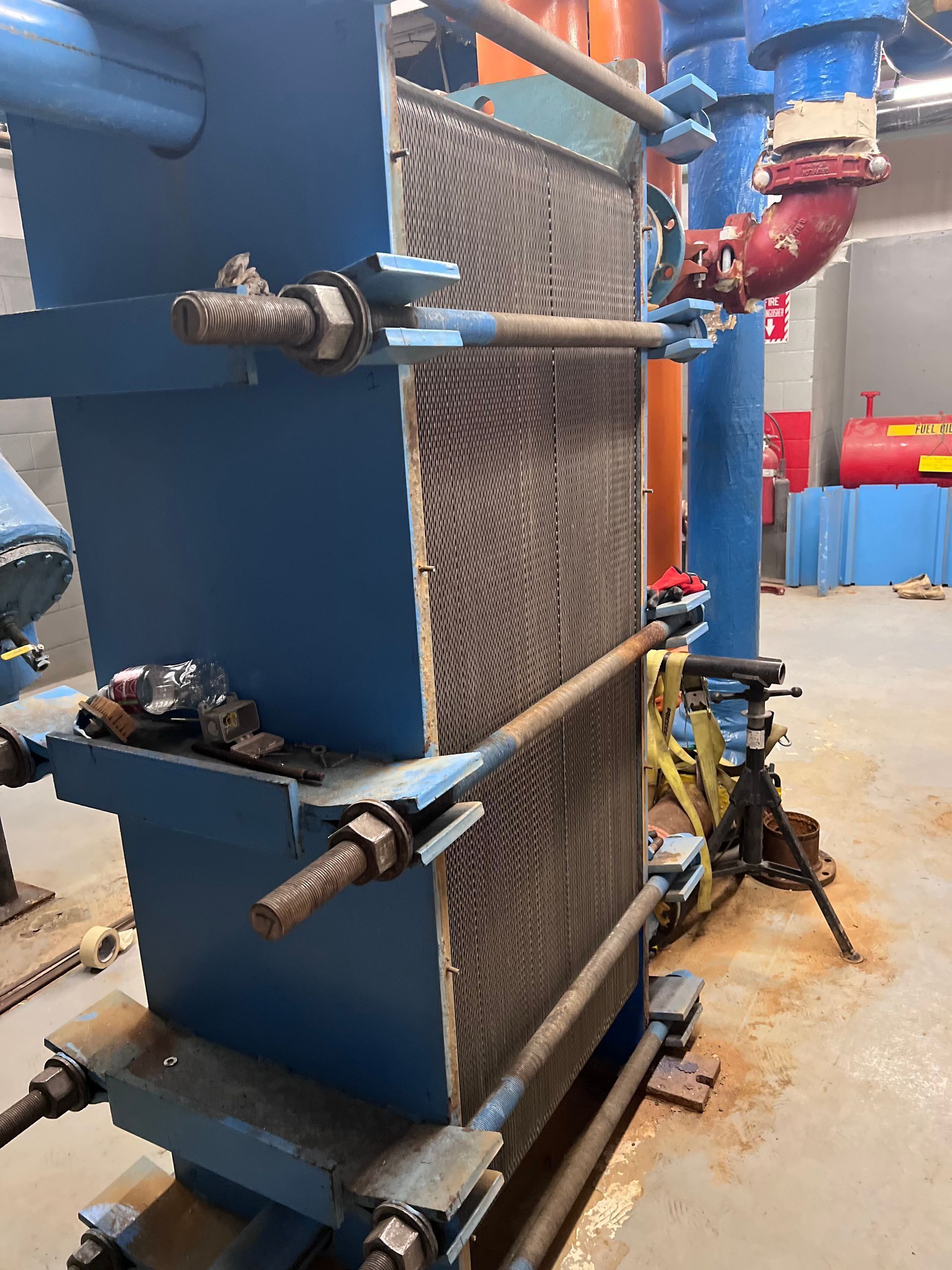 A large blue machine is sitting in a room with pipes.