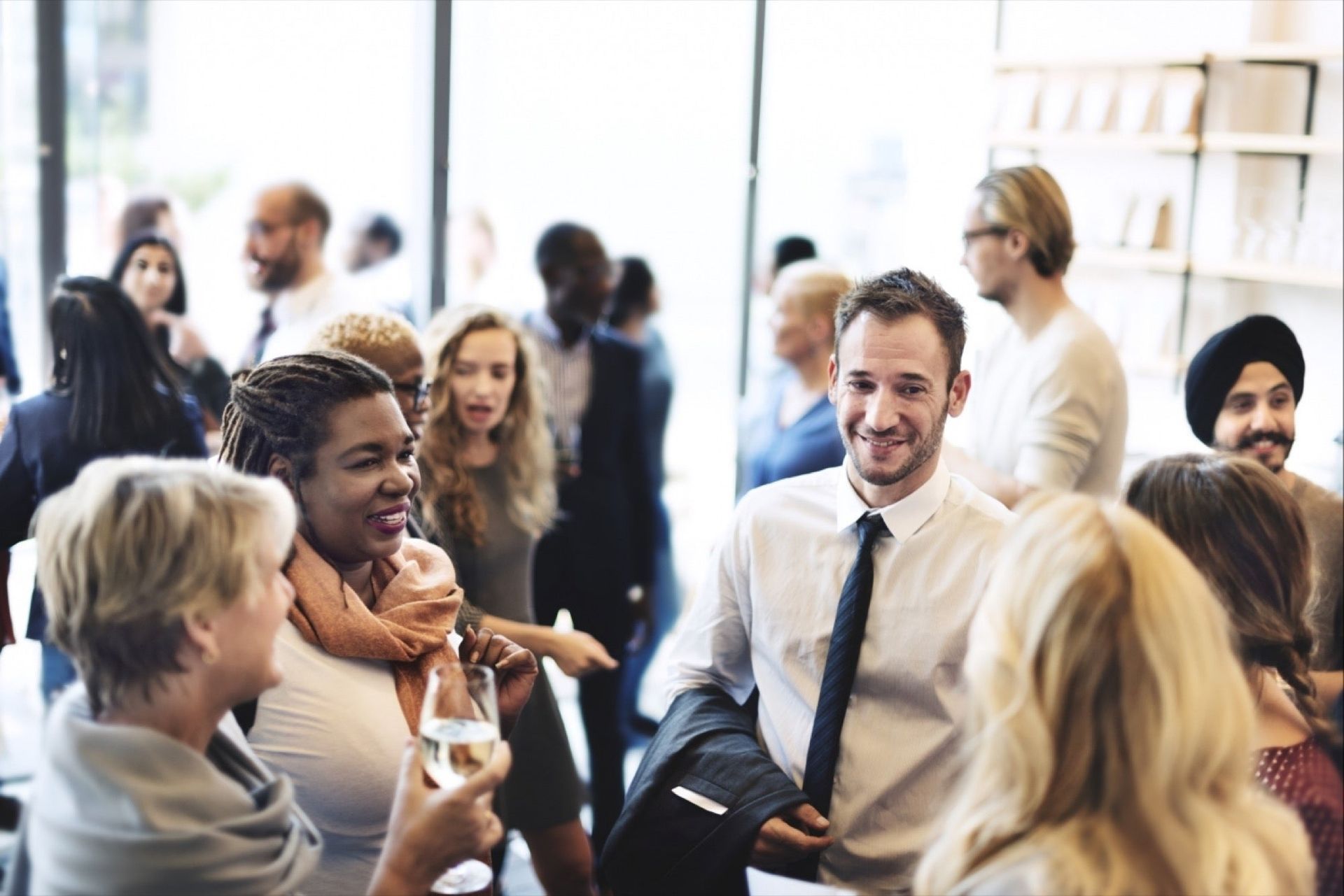 Group of people socializing at an event, with diverse ethnicities, indoors. Several are smiling, some holding drinks.