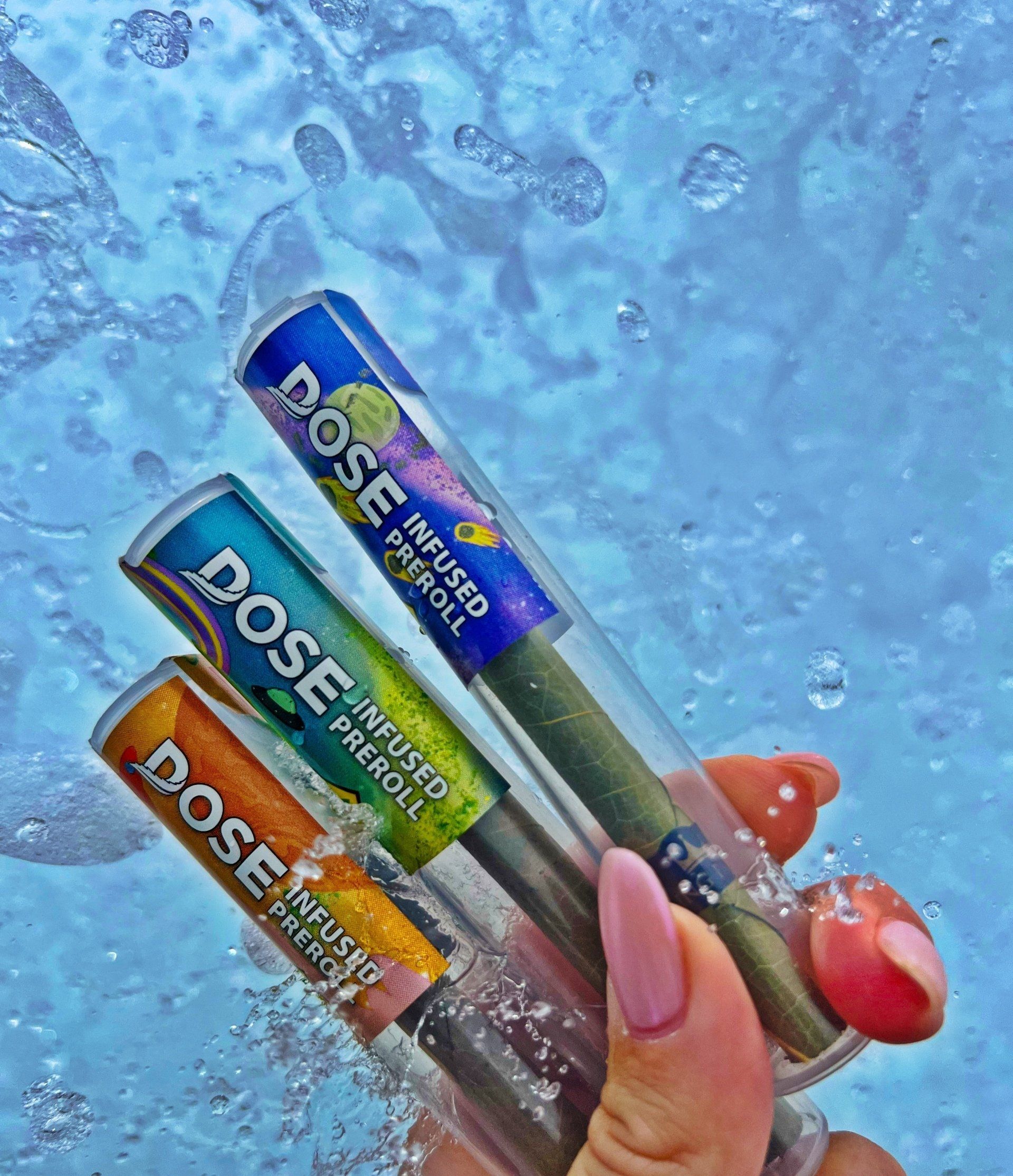 A person is holding three tubes of dose infused pre roll