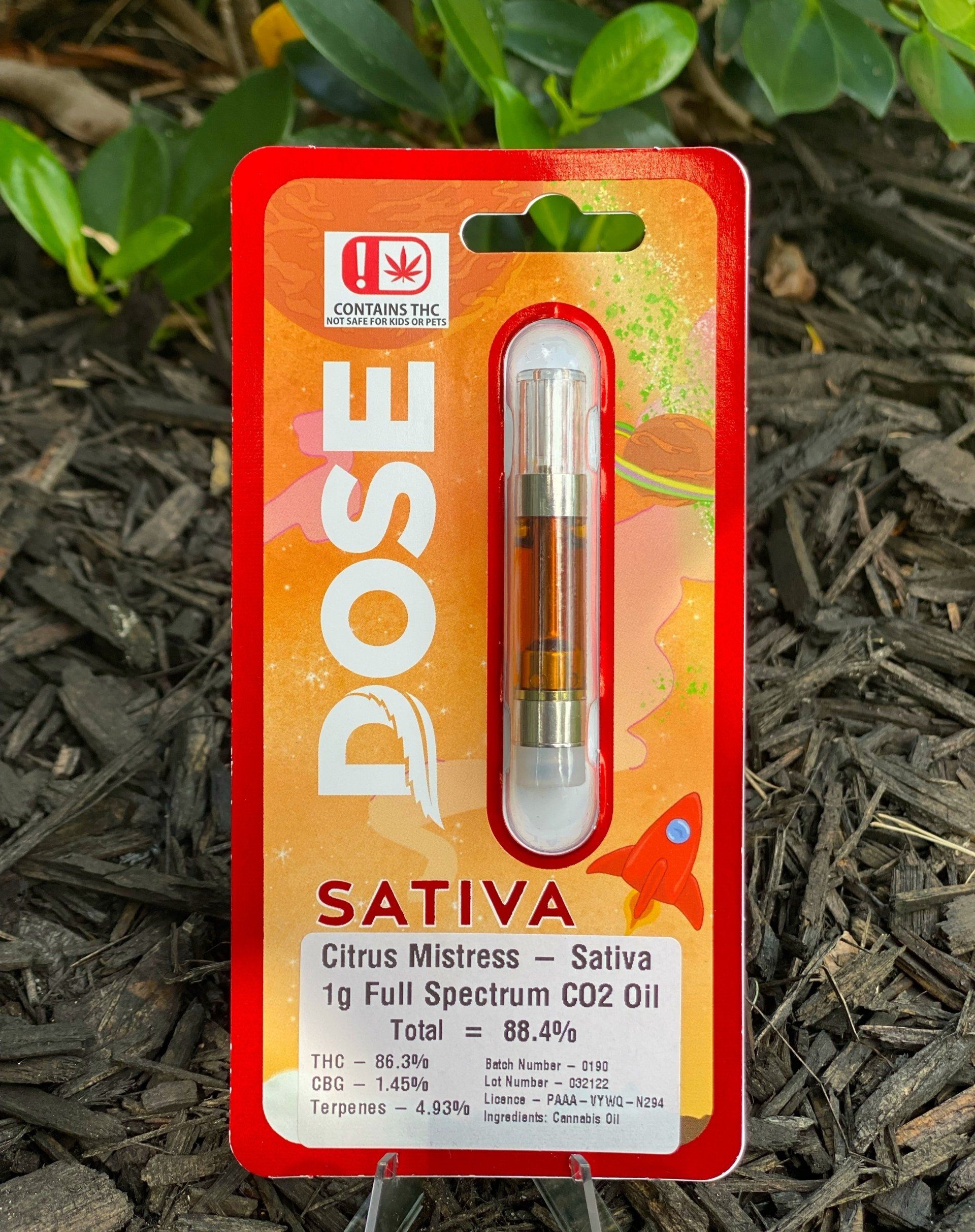 A dose sativa cartridge is sitting on top of a pile of mulch.