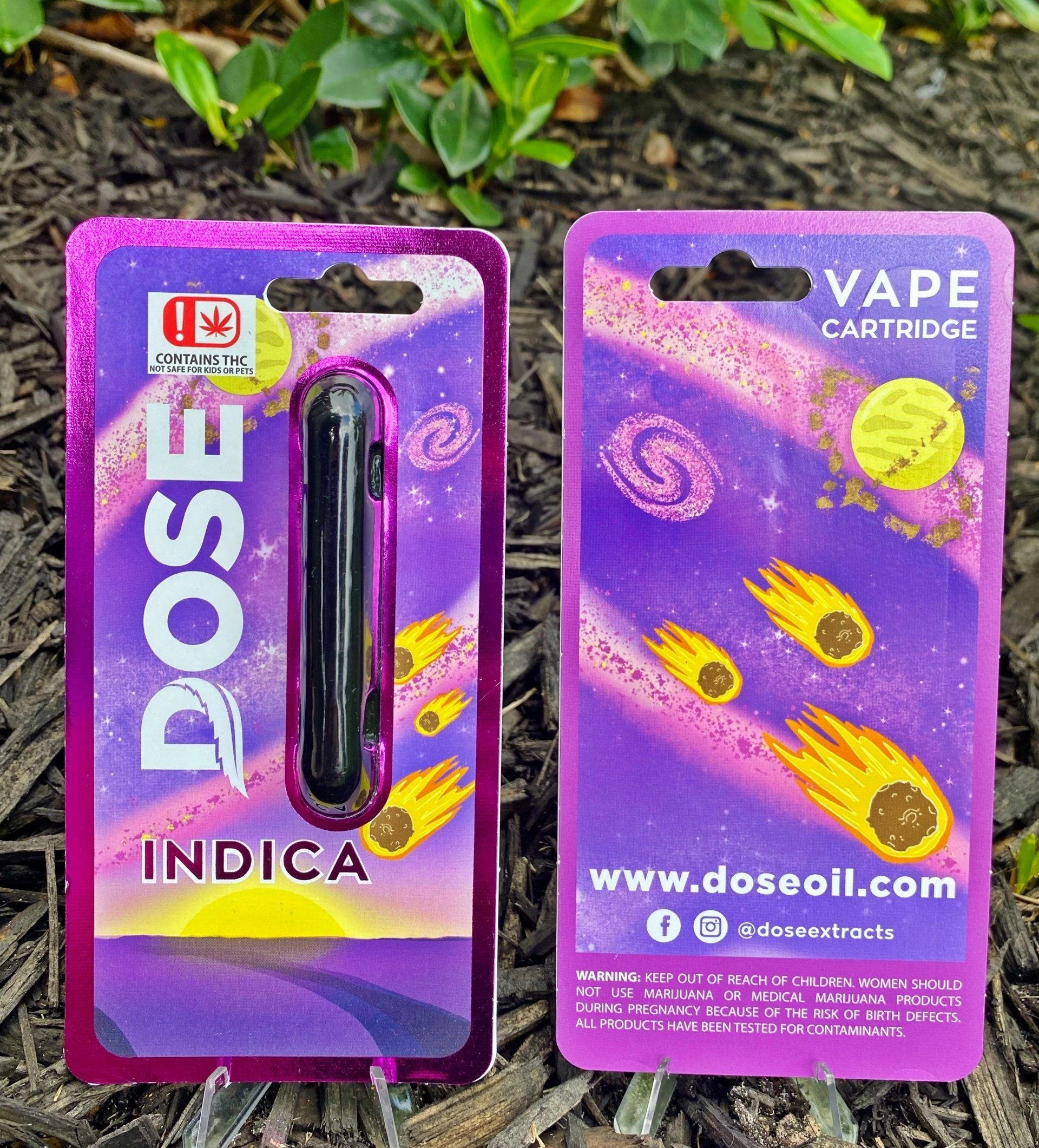 A dose indica vape cartridge is sitting on top of a pile of mulch.