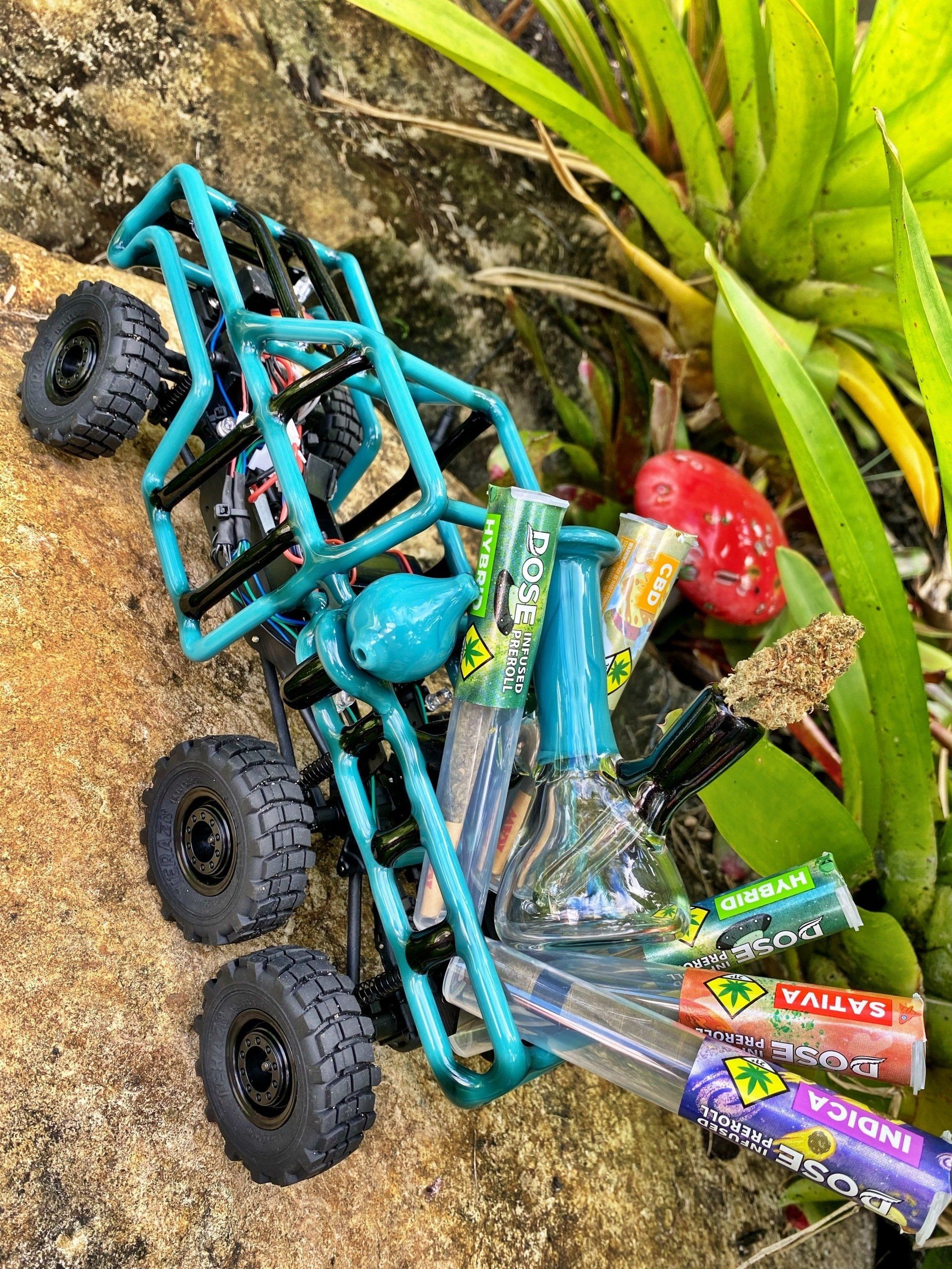 A toy truck is sitting on top of a rock next to a plant.