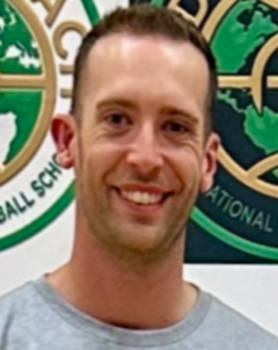 A man is smiling in front of a sign that says national ball school