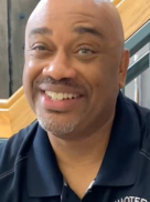 A bald man with a beard is smiling and wearing a black shirt.