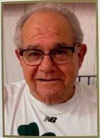 A man wearing glasses and a white shirt with a clover on it.