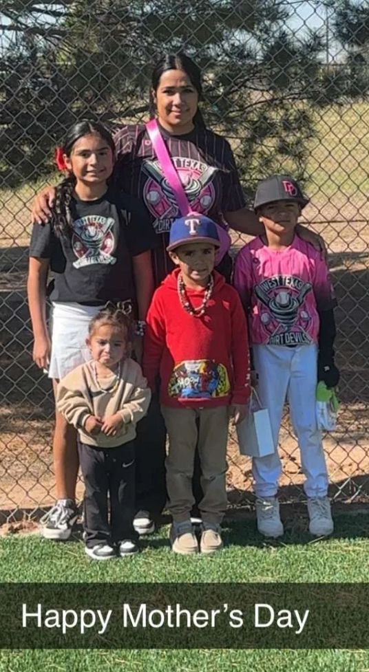 A woman and five children pose for a Mother's Day photo, smiling in front of a fence. The woman wears a pink sash.