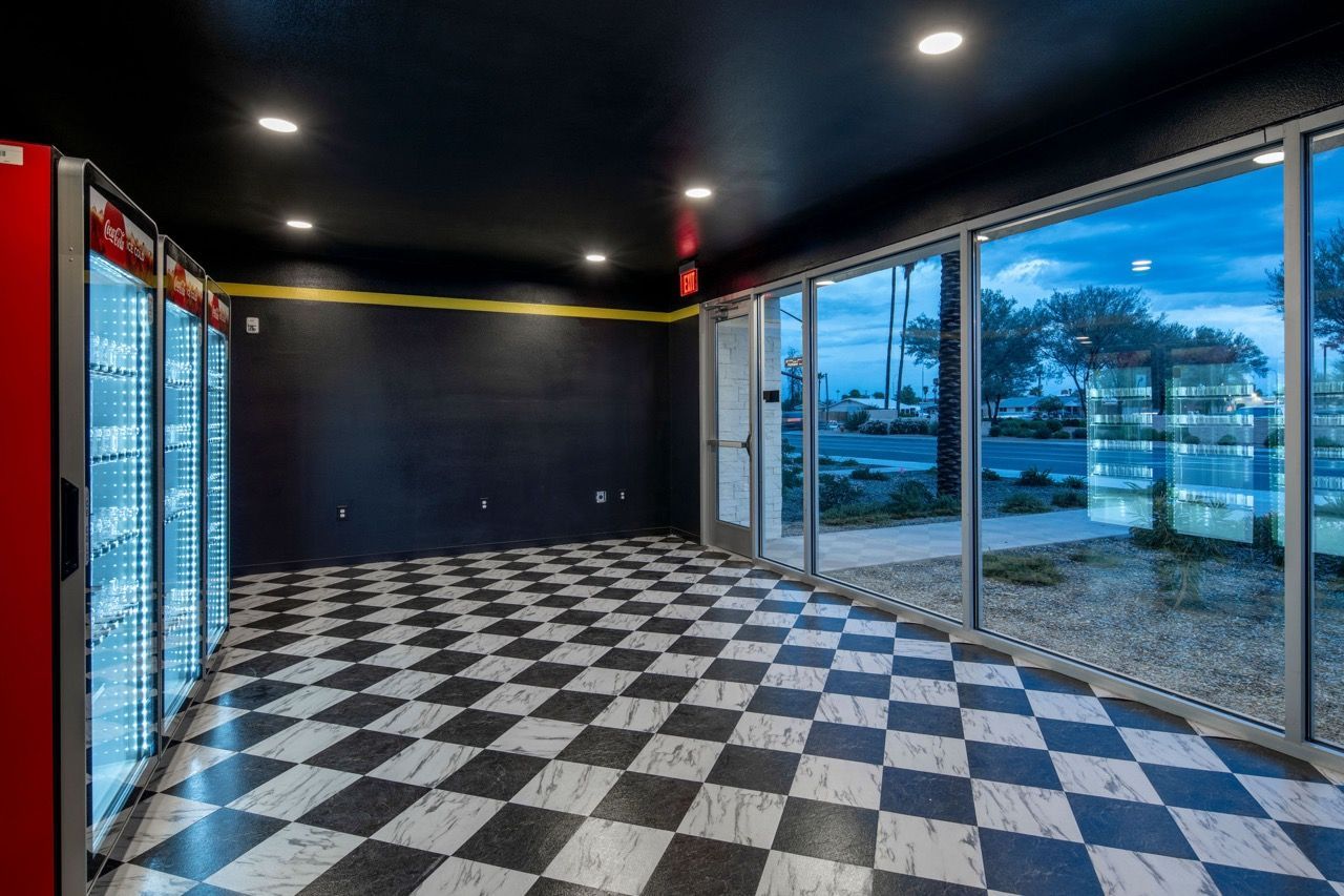 Indoor community lounge with a black-and-white checkered floor, vending machines, and large glass windows.