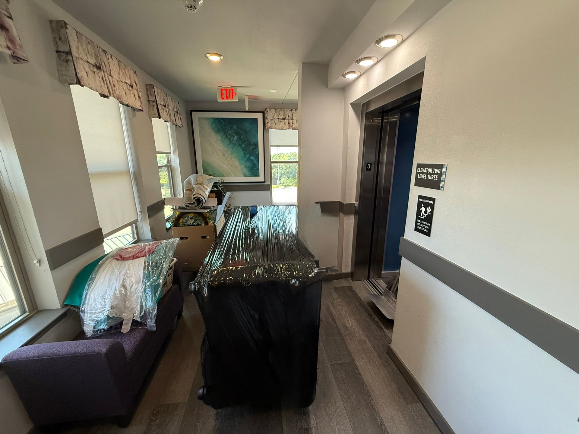 Hallway with a purple couch, elevator, art, and a covered table.