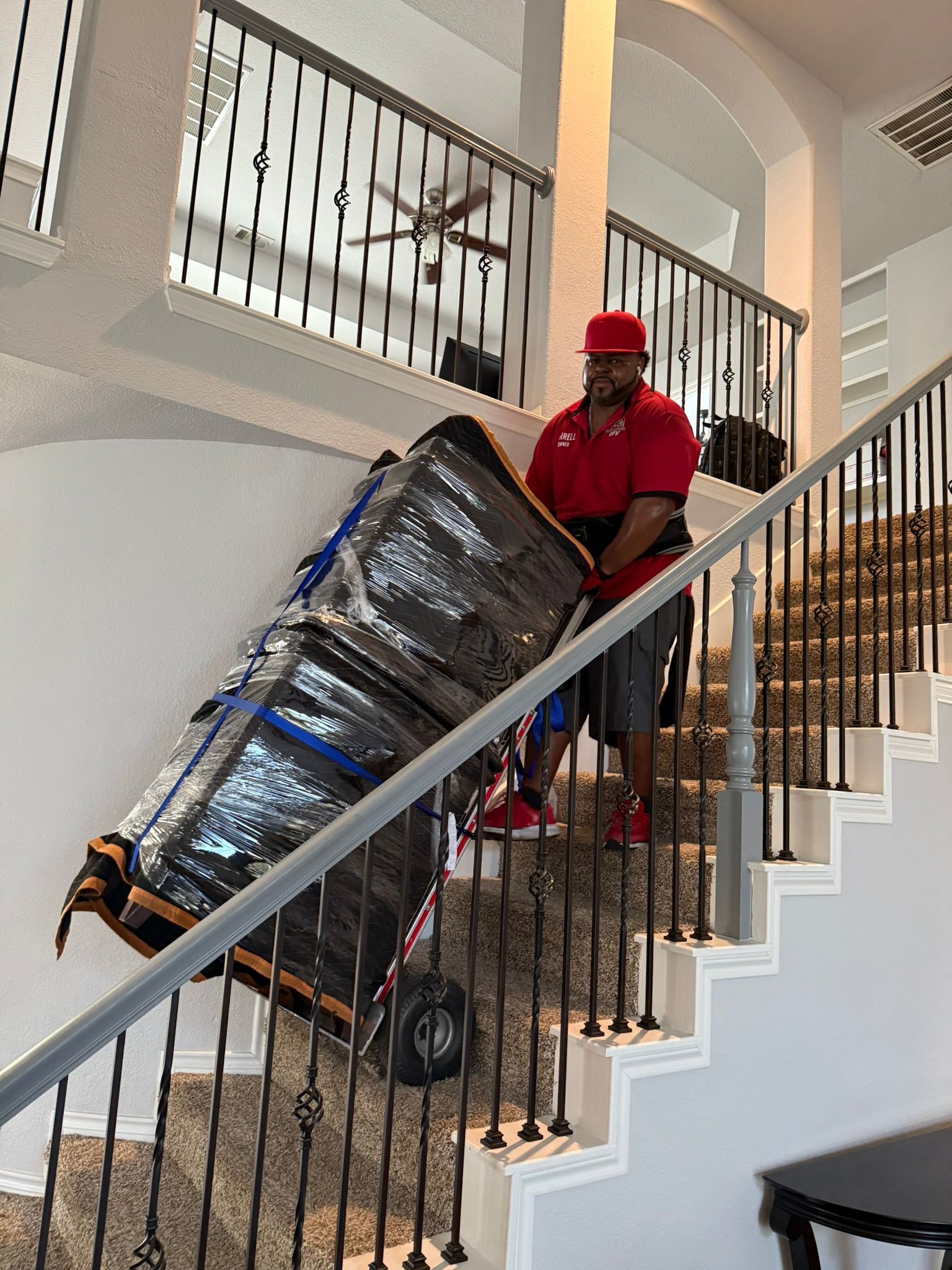 Man in red shirt carrying a large, wrapped object up a staircase with ornate metal railings.