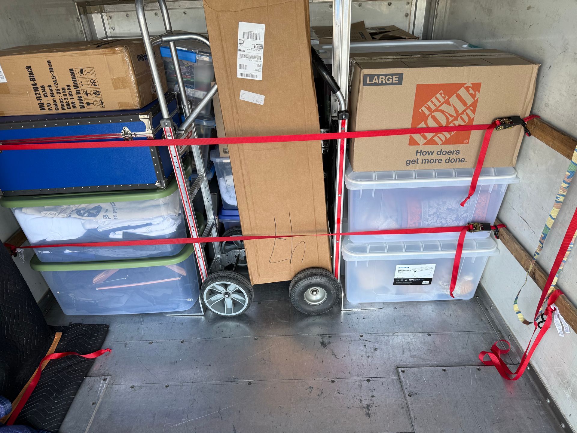 Inside a moving truck, boxes and totes are secured with red straps.