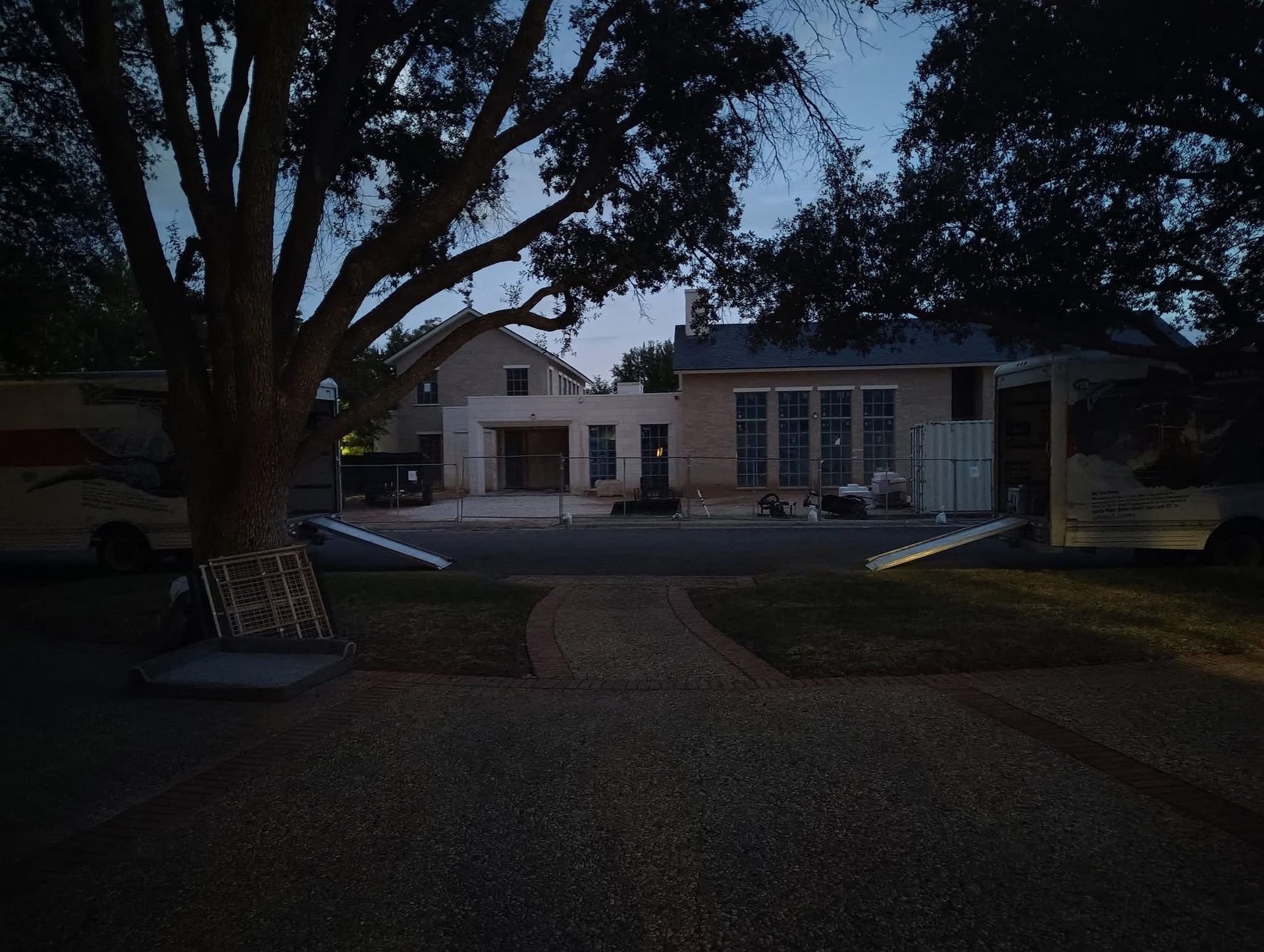 A house at dusk with a tree in the foreground and a gravel path leading to the entrance.