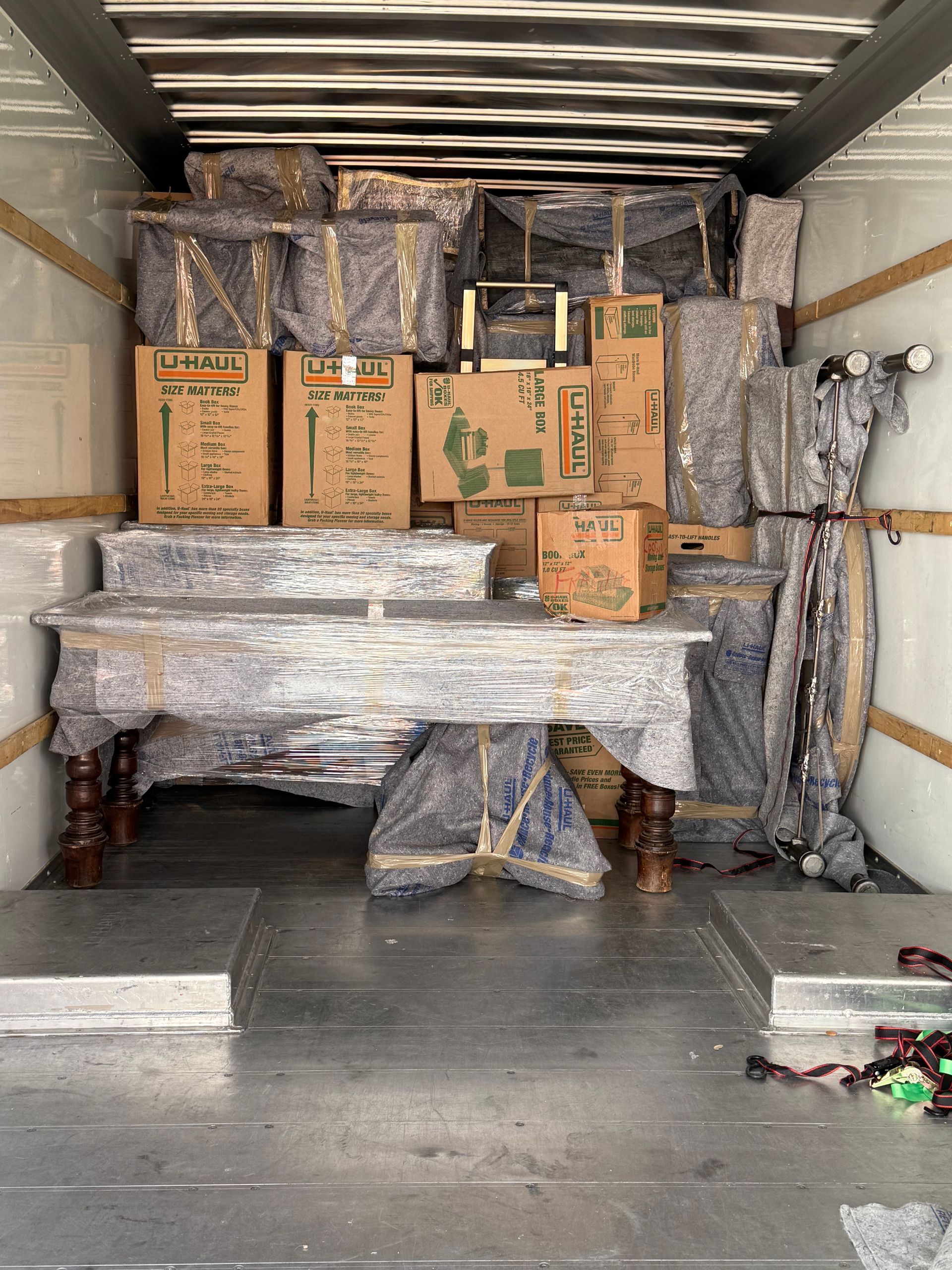 A packed moving truck interior: furniture and boxes wrapped in plastic are stacked tightly.