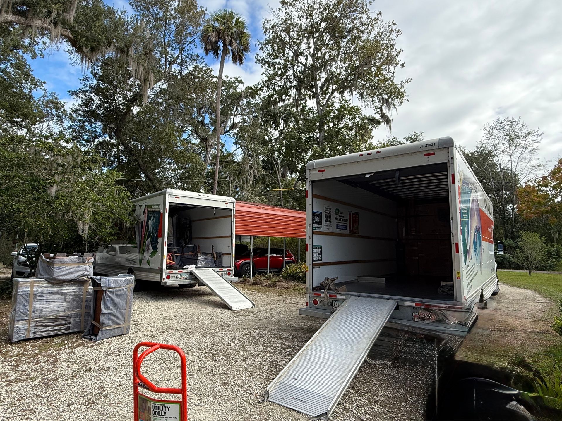 Two U-Haul trucks with ramps open, packed boxes, and trees in background.