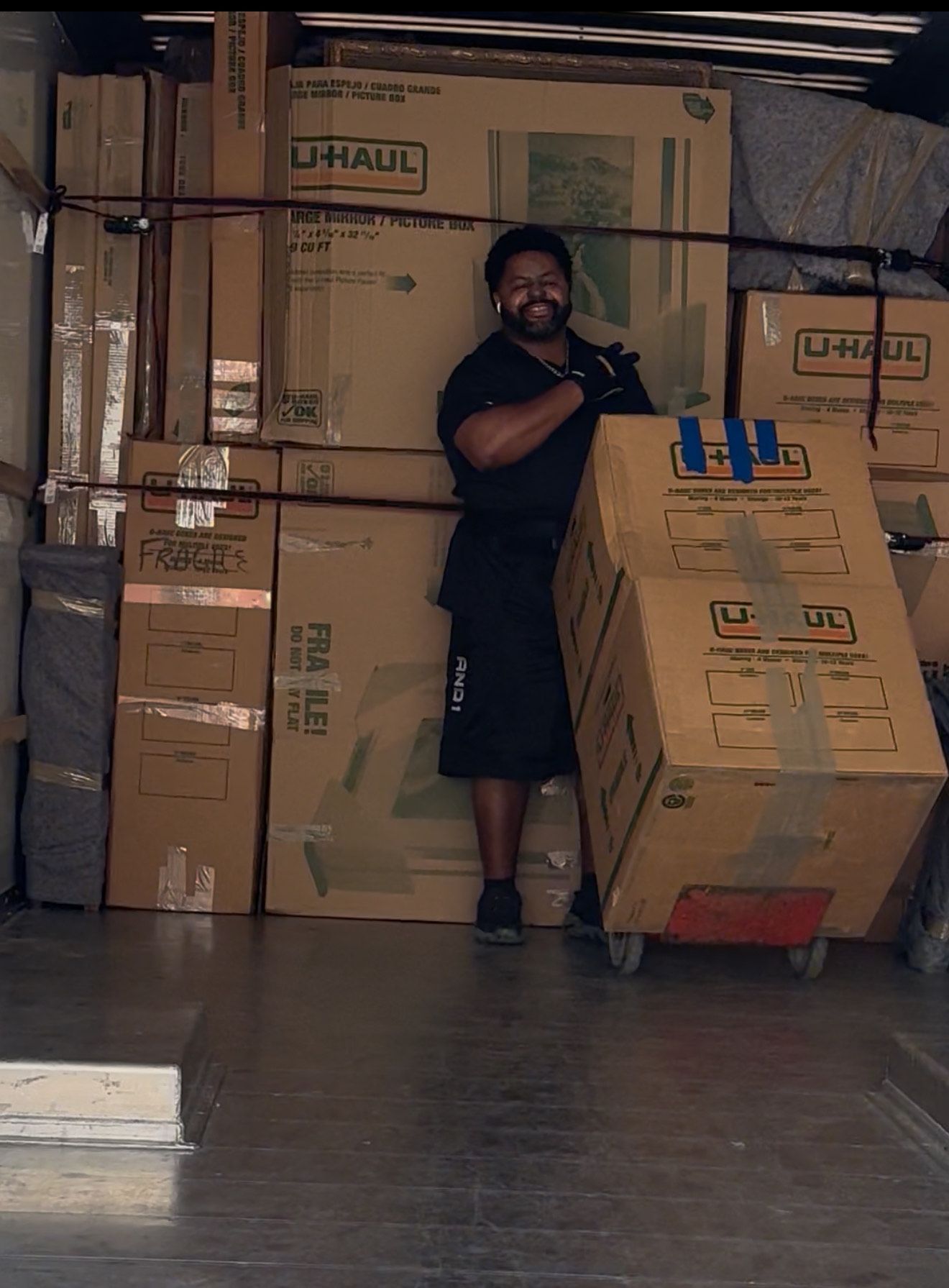 Man smiling, pushing a box on a dolly inside a packed U-Haul truck.