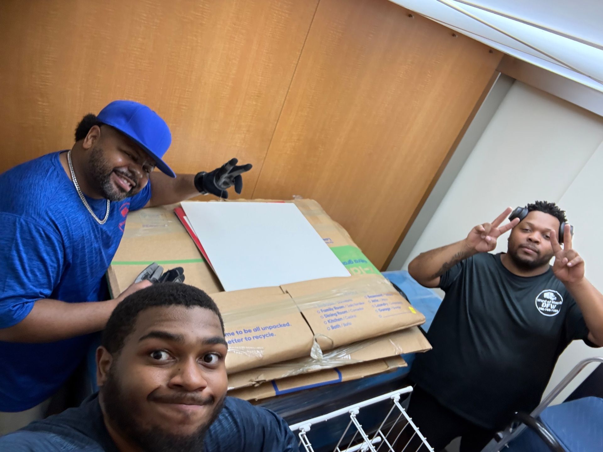Three people smiling near stacked cardboard boxes indoors. 