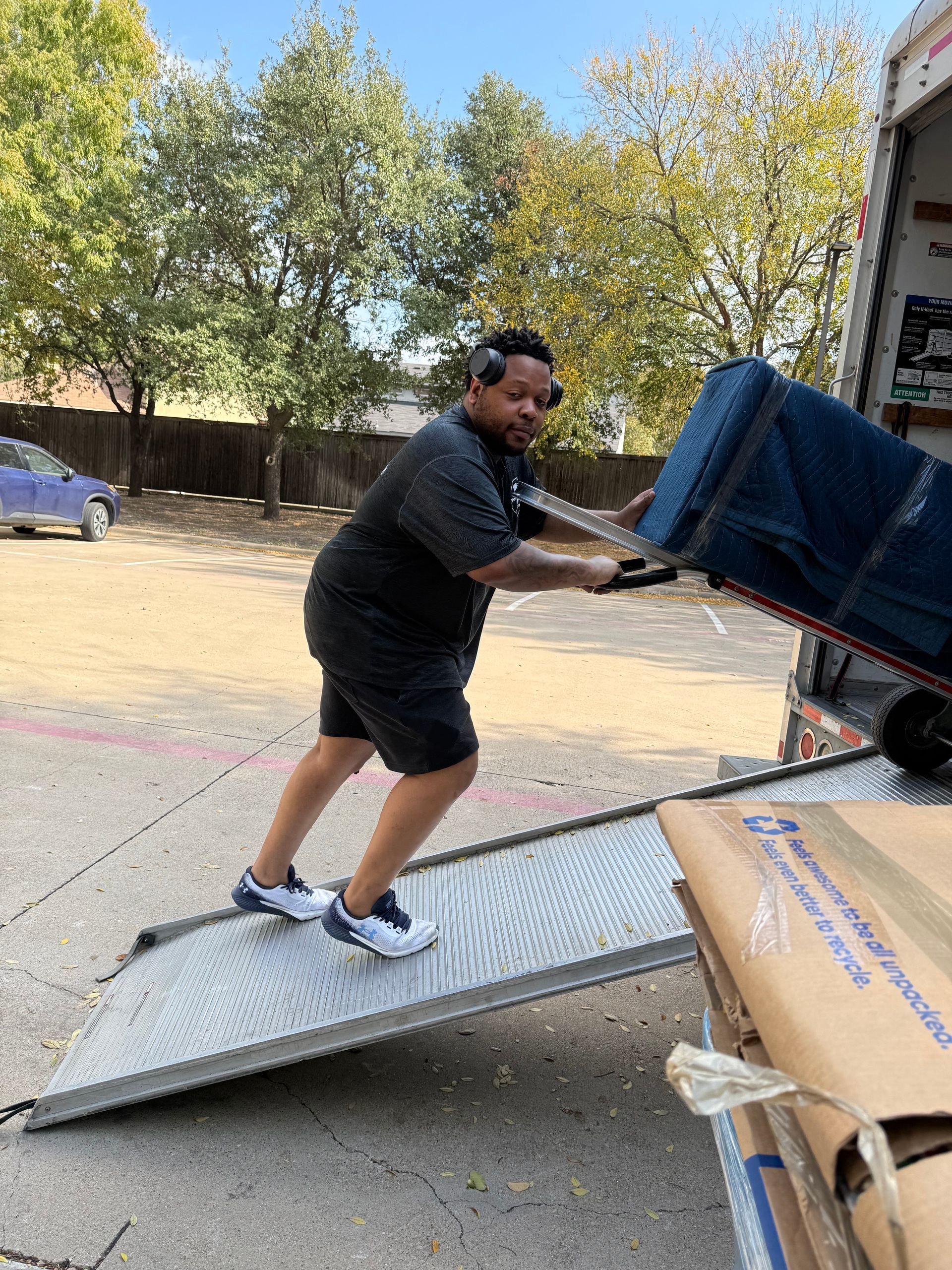 Man pushing a heavy cart with furniture up a ramp into a truck.