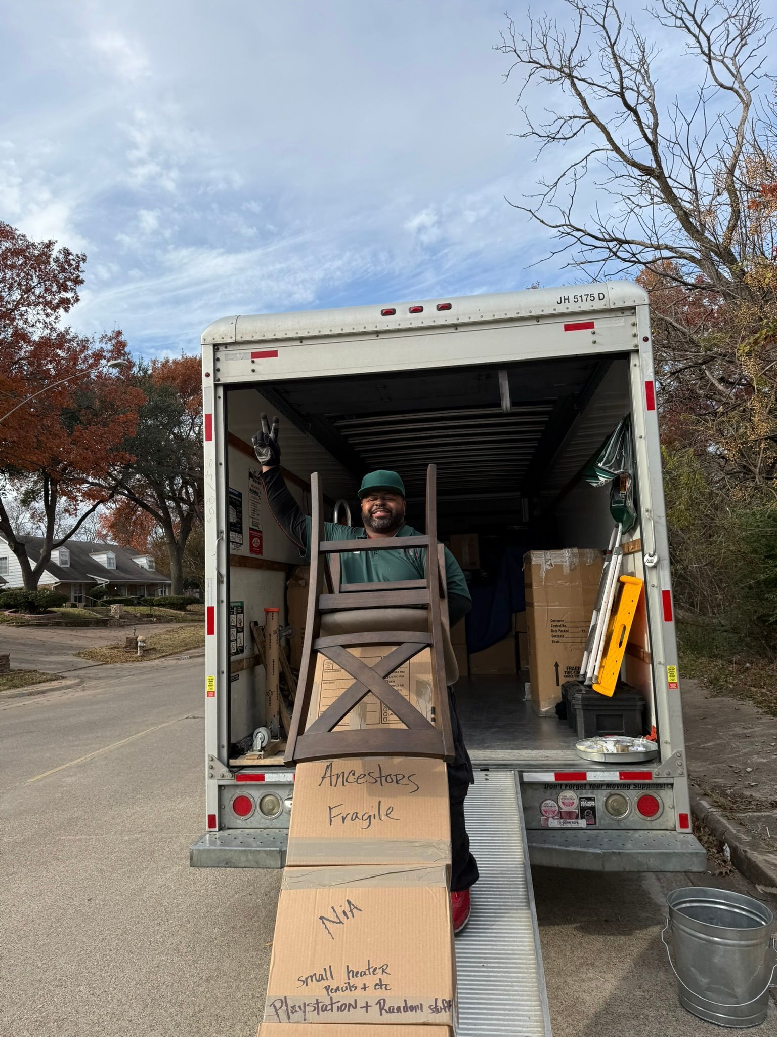 Man carrying a chair out of a moving truck onto a ramp. Boxes in the truck, outdoor setting.