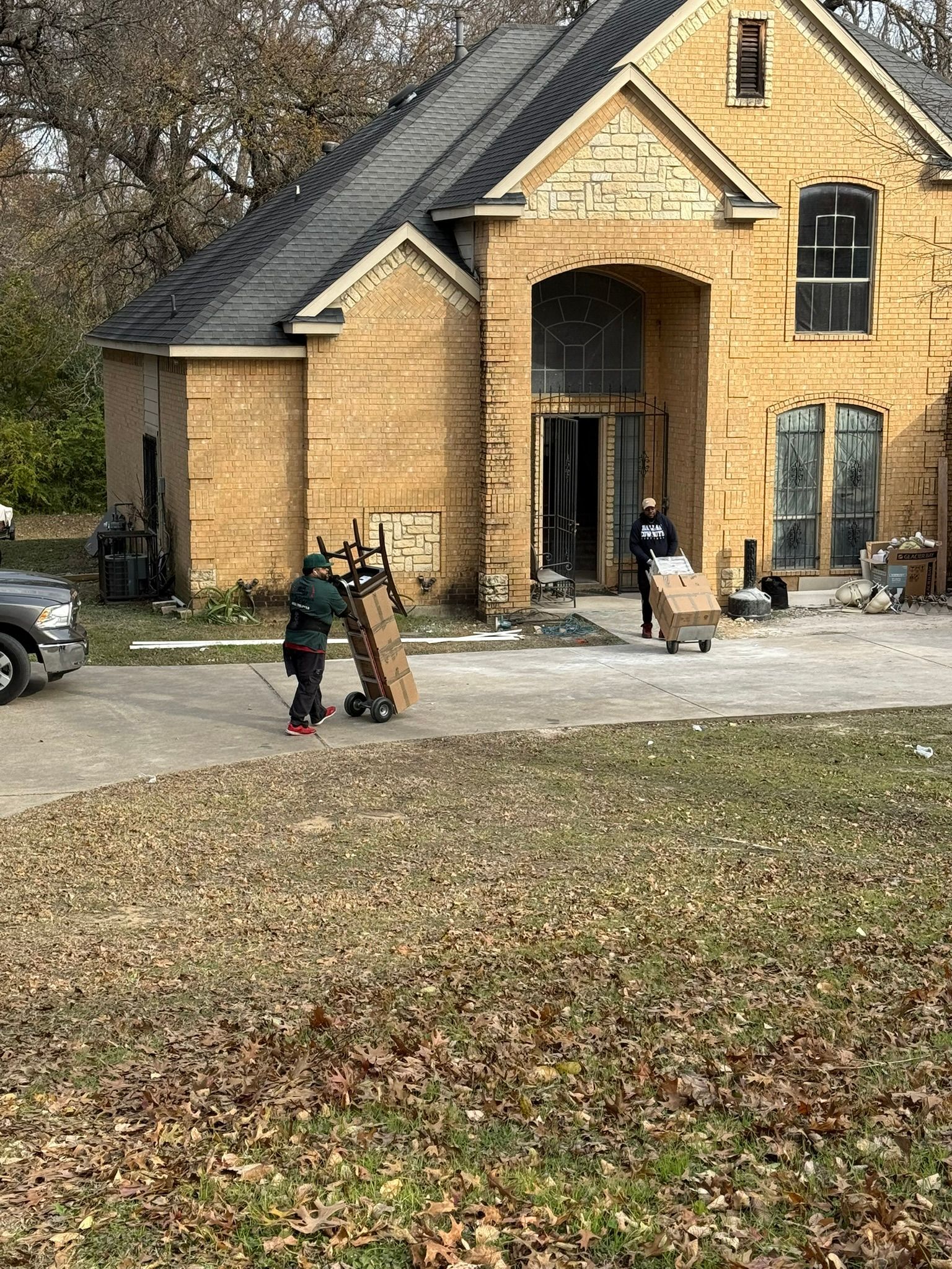 Movers unloading boxes at a two-story house with tan siding and a dark roof.