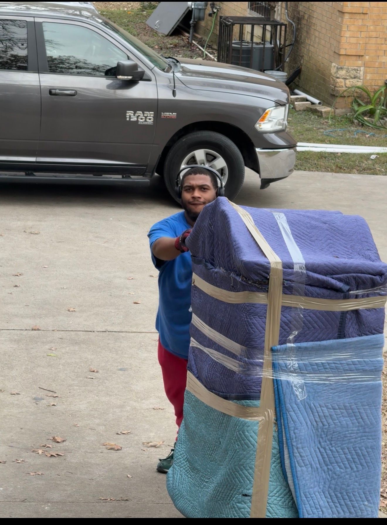 A person in a blue shirt and red pants moves a large, wrapped object with a truck in the background.