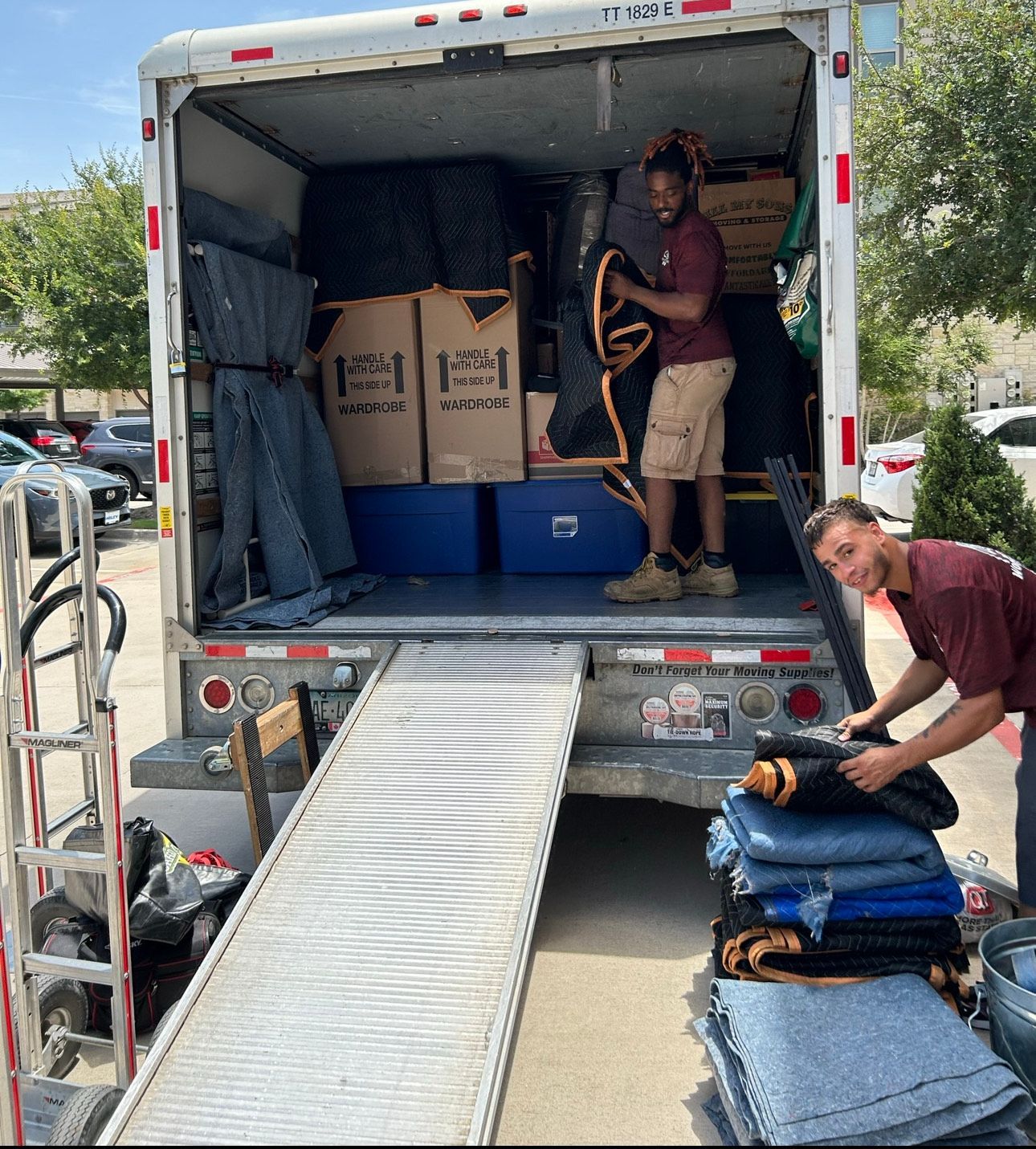 Two movers loading a moving truck. One on ramp, other inside, with furniture pads and boxes.