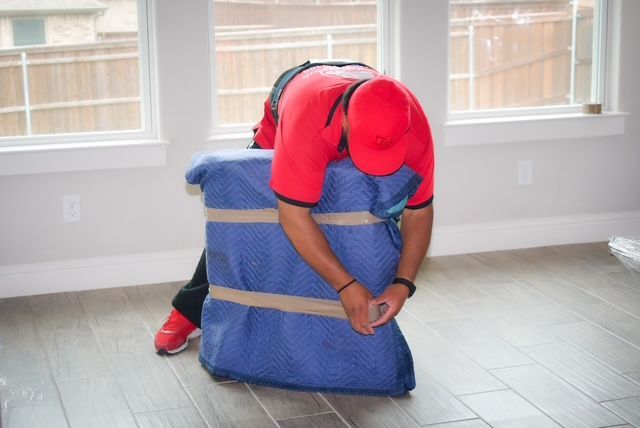 Worker in red shirt securing a blue padded item with straps on a tiled floor near windows