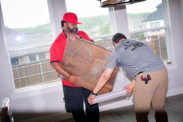 Two workers carrying a large board indoors near windows