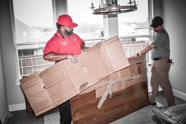 Two movers carrying a large cardboard box through a home doorway