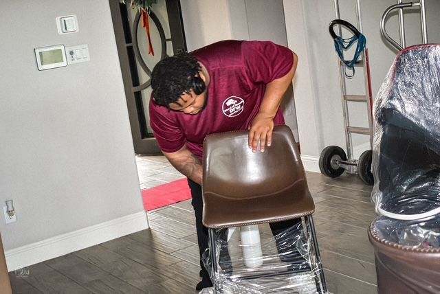 Person leaning over a chair in a room with plastic-covered furniture and cleaning supplies nearby
