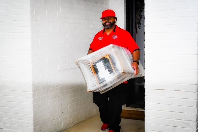 Delivery worker in a red uniform carrying a boxed package through a doorway