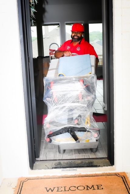 Delivery worker pushing a wrapped cart through a doorway onto a welcome mat