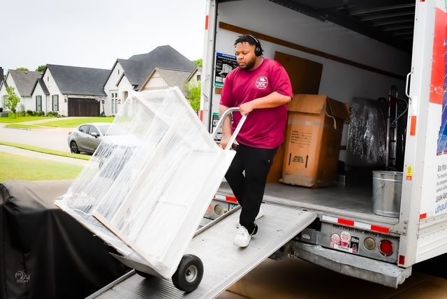 Mover unloading a white cart from a box truck ramp on a residential street