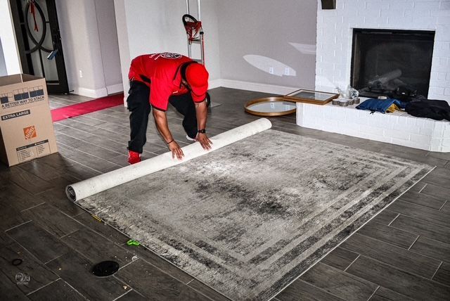 Worker rolling out a gray carpet in a living room with a fireplace and dark tile floor