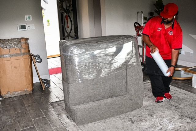 Worker in red uniform moving a wrapped mattress or cushion through a garage.