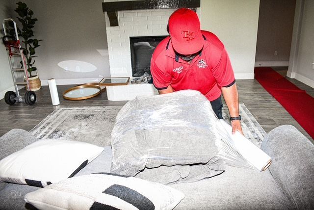 Person in red cap arranging a gray cushion on a couch in a bright living room
