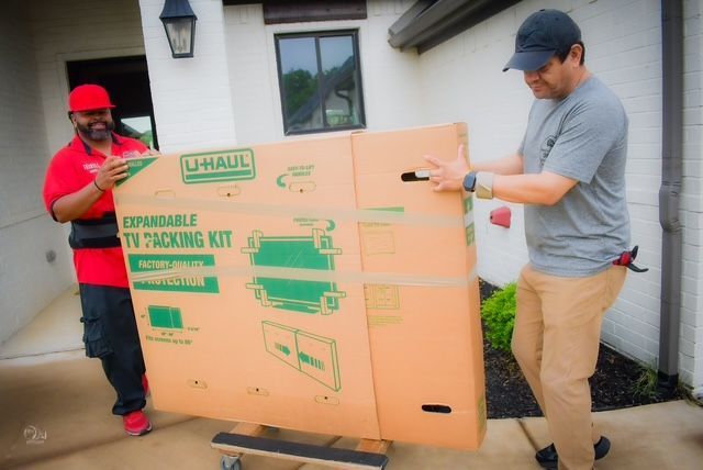 Two workers unloading a large U-Haul box from a truck outside a house