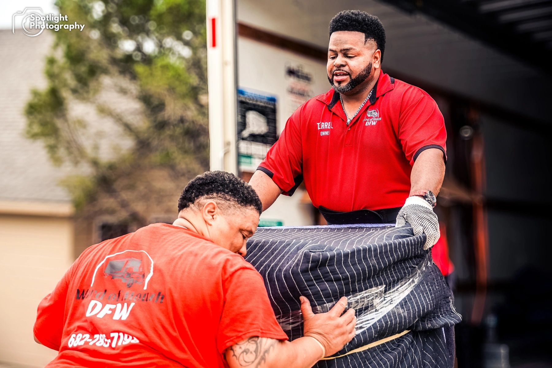 Two men in red shirts are loading a couch into a truck.
