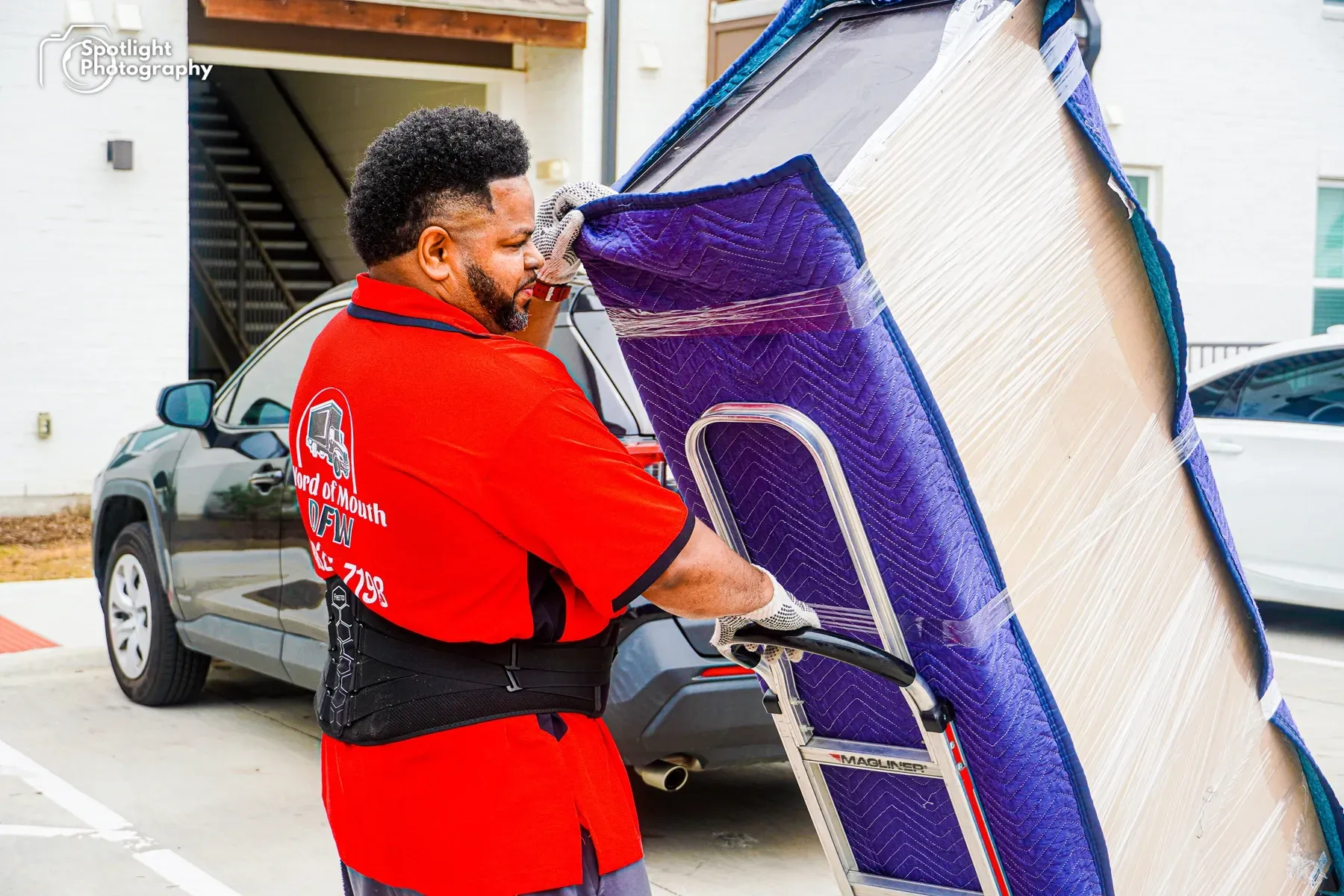 A man in a red shirt is pushing a mattress on a dolly.